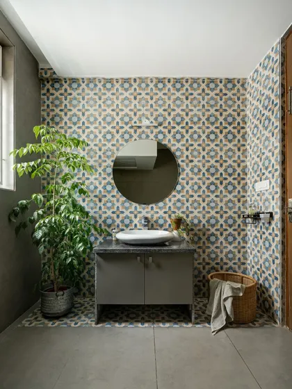This bathroom uses bold patterned wall tiles to create a vibrant feature wall. Paired with a simple grey vanity and concrete-finish walls, the design is stylish and functional.