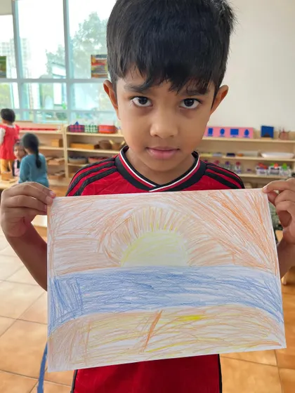 A child holds up his drawing of a sunrise, a symbol of hope for the new year. Art is a powerful medium for children to express their feelings and ideas.