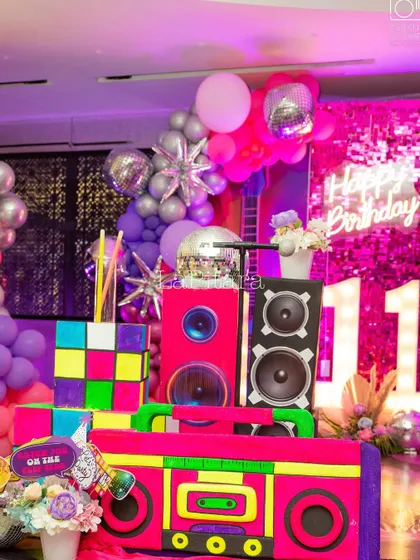 A collection of retro props, including a boombox, speakers, and a neon 'Happy Birthday 11' sign, all contributing to the disco vibe.
