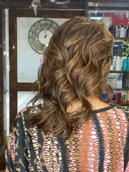 A global color base with added highlights gives this client's hair a refreshed and vibrant look. The soft curls add volume and showcase the multi-tonal effect.
