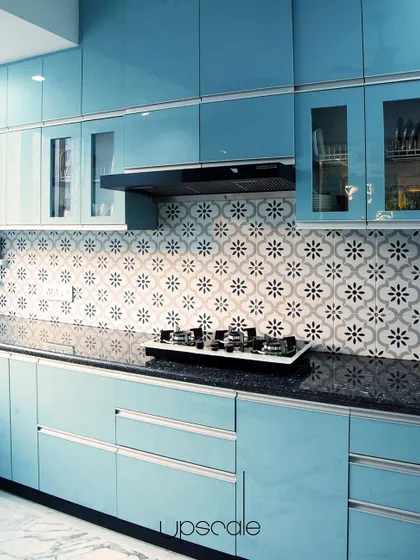A kitchen with a touch of wonder. Powder blue lacquered glass cabinets are paired with a patterned tile backsplash and a black granite countertop, creating a space that is both playful and functional.