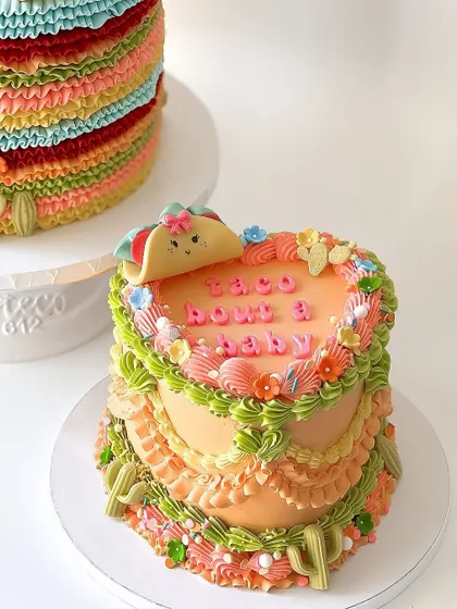 A fun and unique vintage-style cake with a "Taco 'bout a baby" theme. This heart-shaped cake features colorful piped ruffles and a cute fondant taco on top.