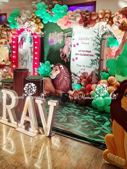 A lush and detailed jungle stage for a baby welcome party, with a green foliage floor, 3D lion props, and marquee letters spelling out the baby's name.
