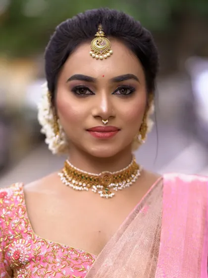 A soft and elegant bridal portrait. The makeup features a subtle smokey eye and a natural base, paired with a pink saree for a fresh and modern take on the traditional look.