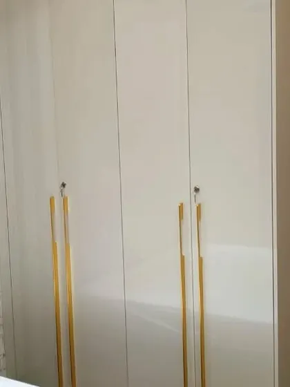 A high-gloss white wardrobe with statement-making long golden handles, adding a touch of glamour and luxury to the bedroom.