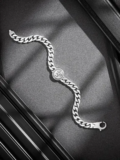 An elegant flatlay of an Om-symbol bracelet from Orionz Jewels. The play of light and shadow across the textured black panels creates a sophisticated and almost architectural composition.