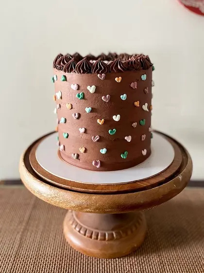 A tall chocolate cake that's as cute as it is delicious. The rich chocolate buttercream is covered in tiny, multi-colored piped hearts, making it a sweet and simple design for any birthday.