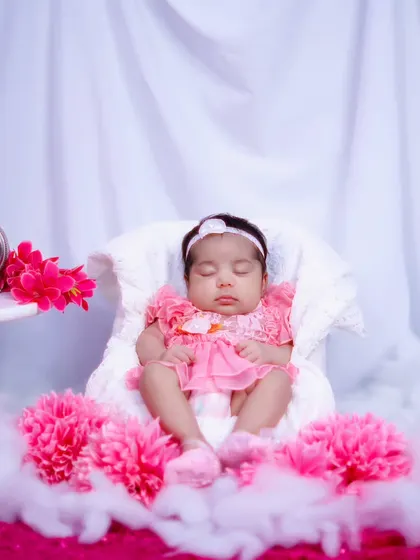 A wider shot of the one-month-old baby girl in her pink dress, surrounded by soft clouds and flowers in a dreamy setup.