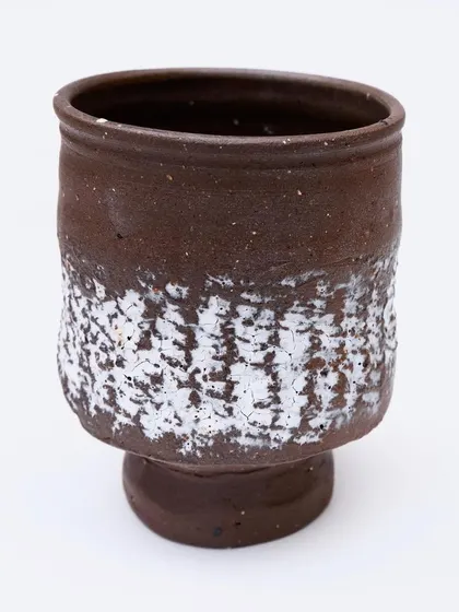 A tea bowl with a unique 'crawl' glaze. The thick white glaze has pulled apart during firing to reveal the dark clay underneath, creating a texture that feels like lichen on a rock.