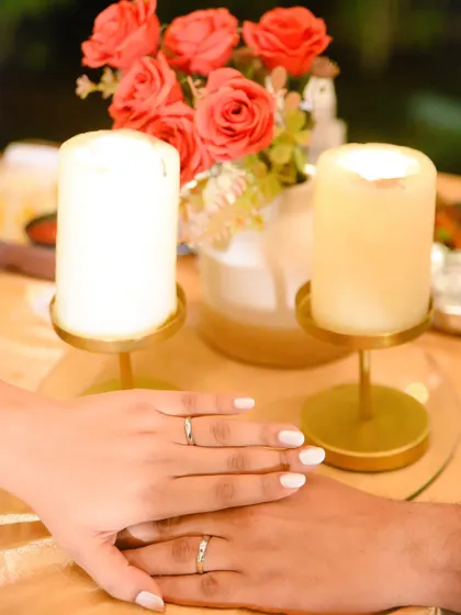 A close-up shot of the couple's hands with their engagement rings, set against a romantic backdrop of candles and roses.