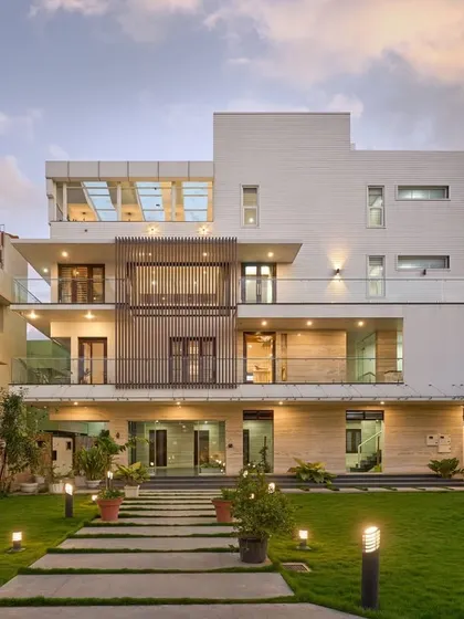 The facade of 'Wilasa' is minimalistic, using plaster with horizontal grooves and vertical wooden slats for a modern look. The landscaped pathway leads the eye towards the home, enhancing its grand entrance.