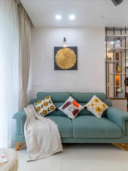 A comfortable and stylish living room with a teal sofa and vibrant cushions. The gold wall art and modern partition add touches of elegance and personality to the space.