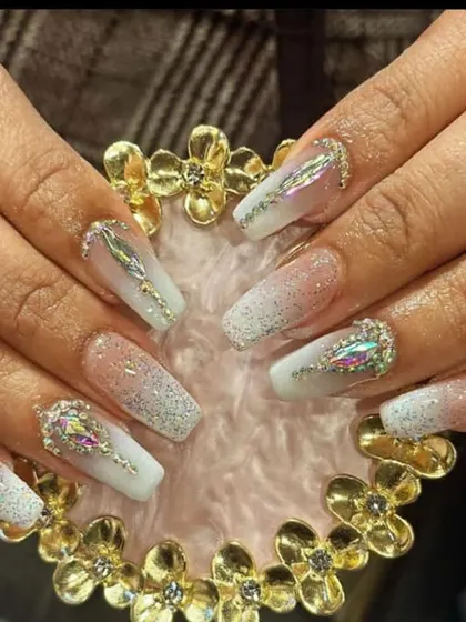 An icy, glamorous look with a white glitter ombre on long coffin nails, featuring large, iridescent multi-faceted crystals as statement pieces.