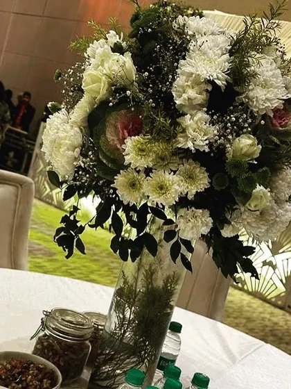 A close-up of a table centerpiece, featuring a large arrangement of white chrysanthemums and greenery, adding a touch of freshness to the guest tables.