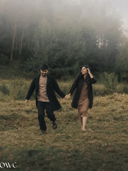 A couple walks hand-in-hand through a misty, atmospheric landscape, creating a moody and cinematic pre-wedding photograph.