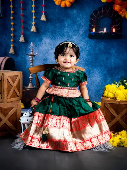 A full-length portrait of a little girl in a gorgeous traditional pattu pavadai. Her sweet smile and the vibrant colors of the outfit make this a cherished cultural photograph.