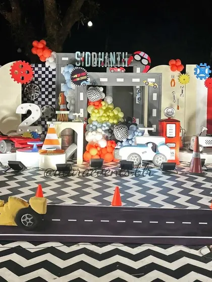 A complete race car-themed birthday stage. The setup features a road-patterned floor, a gas station prop, and large car cutouts, creating an immersive environment for a little car enthusiast's second birthday.