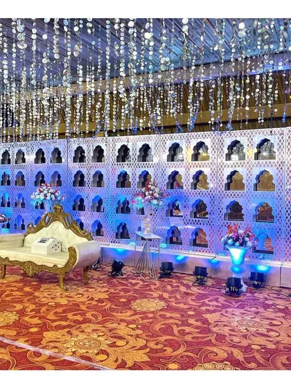 A full stage setup featuring the white 'jharokha' wall. The hanging crystal ceiling and blue uplighting create a magical, winter-wonderland effect.