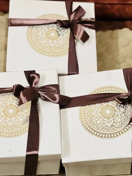 A trio of elegant white gift boxes with a gold mandala design, tied with a luxurious brown satin ribbon.