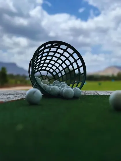 A basket of golf balls spilled onto the practice green, with the beautiful course and cloudy sky in the background. It's a perfect day for practice, rain or shine.