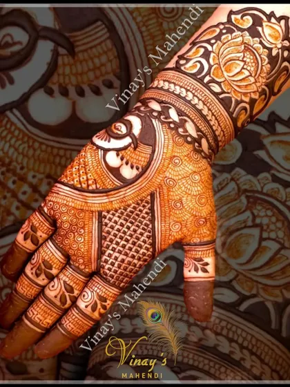 A close-up of a designer short-hand mehndi, focusing on the intricate peacock and floral work on the back of the hand.