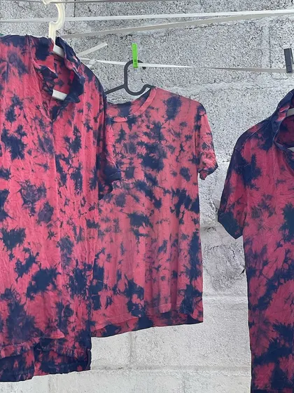 A collection of red and indigo tie-dyed shirts. The contrast between the madder red and deep indigo creates a striking visual, with each garment having its own unique pattern.