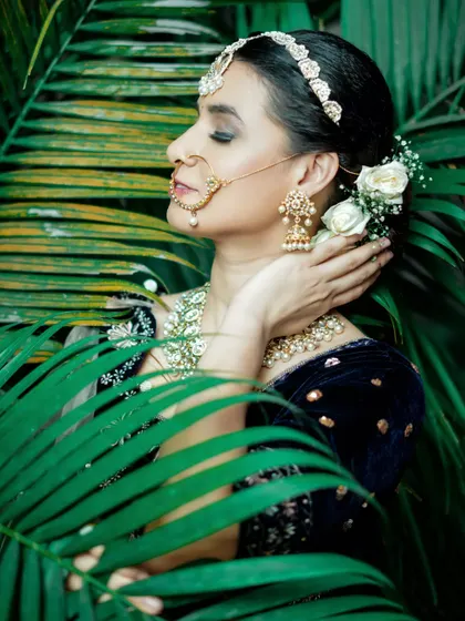 A beautiful profile shot amidst lush greenery, highlighting the floral hairstyle and elegant makeup.