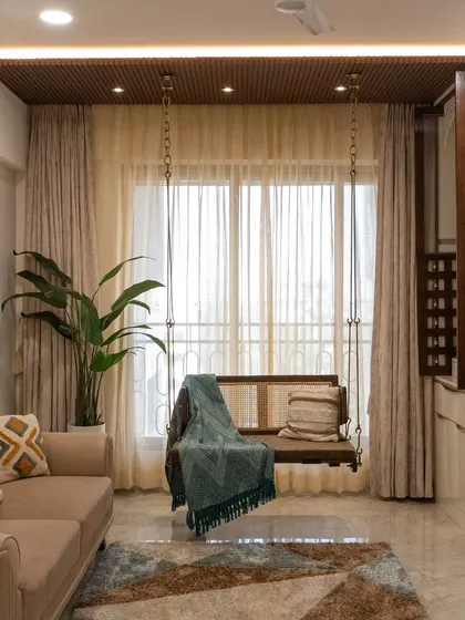 This living room is a fusion of luxury and tradition, featuring a classic wooden swing, a framed mandir, and warm wooden accents.