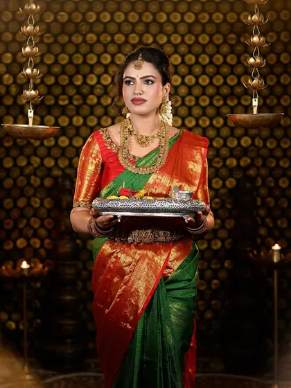 A complete look at a traditional South Indian bride in a stunning green and red Kanjivaram silk saree. The makeup features defined eyes, a bold matte lip, and a flawless base that complements the antique gold jewelry.