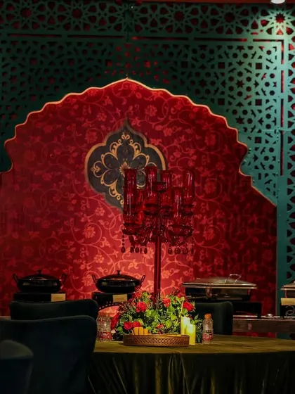 A dining table set before a decorative backdrop of red and green panels. The red glass candelabra centerpiece ties the table setting directly into the larger architectural color scheme.