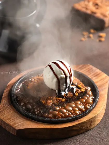 A sizzling brownie on a hot plate, with steam rising and chocolate sauce bubbling, capturing a dynamic and sensory experience.
