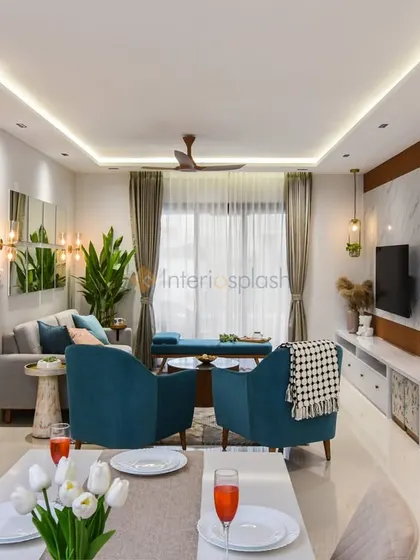 This bright and airy living room uses a light color palette with pops of teal in the armchairs. The false ceiling with strip lighting provides even, ambient illumination throughout the space.