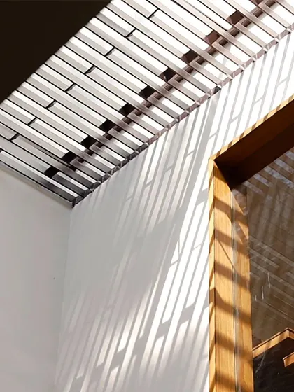 The skylight in the Twin Courtyard House is protected by custom MS rods that act as a security grill. This feature creates a beautiful pattern of light and shadow on the wall, turning a functional element into a design feature.