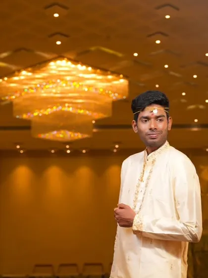 A portrait of the groom in a grand hall, with a stunning chandelier hanging above him.