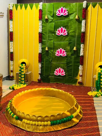 A vibrant Haldi ceremony decoration with a backdrop of banana leaves and marigold flowers, featuring traditional elements like a brass urli for the ceremony.