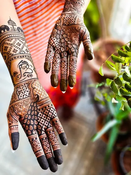 This engagement henna tells a story with traditional symbols. One hand features a prominent Ganesha motif for good luck, while the other includes peacock and elephant elements, all woven into a dense, celebratory design.
