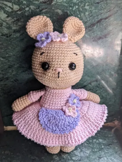 A lovely bunny doll in a pink dress with a purple apron, decorated with tiny flowers.