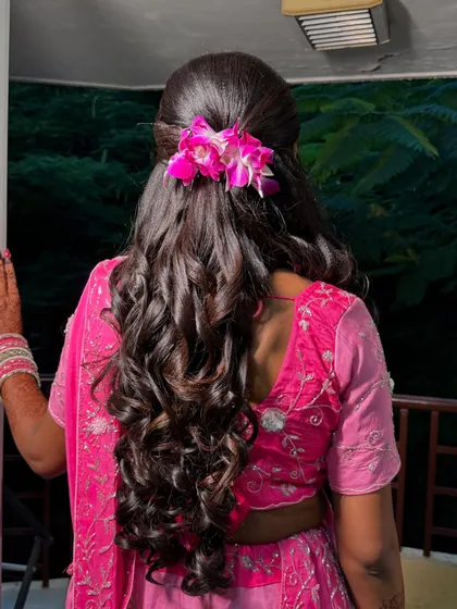 The hairstyle for Meena's engagement. Soft waves adorned with fresh pink orchids create a romantic and modern look.