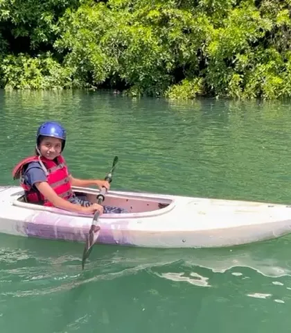 A young girl in a kayak pauses to smile for the camera, with the clear green water of the Kali River around her.