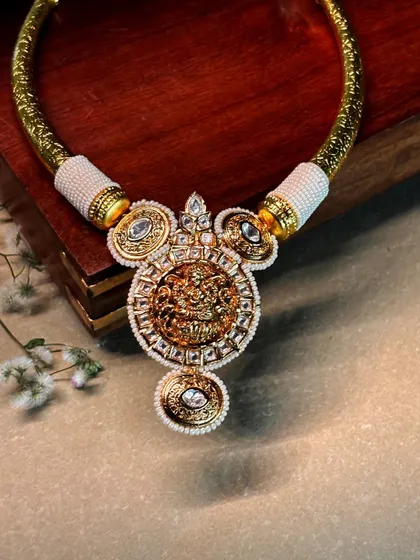 A magnificent temple jewelry pendant on a textured gold-toned hasli, or collar necklace, wrapped in pearls.