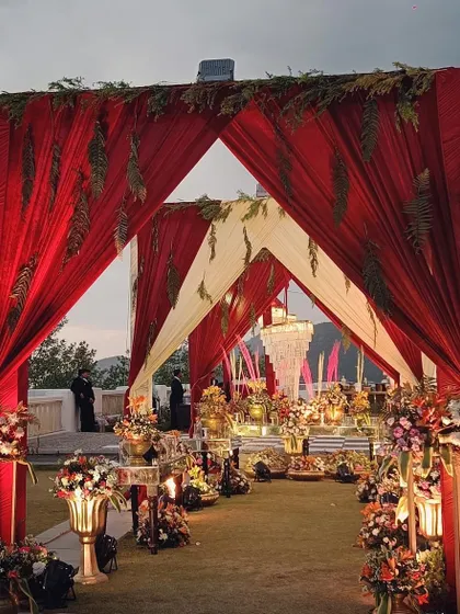 A grand entrance for a mountain wedding, with canopies of red and white fabric leading to an area filled with traditional brass decor and floral arrangements.