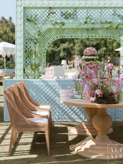 A seating area at the 'Mayfair Luncheon', with a backdrop of pastel blue trellis structures. The combination of natural wood chairs and soft colors created a light and loving mood.