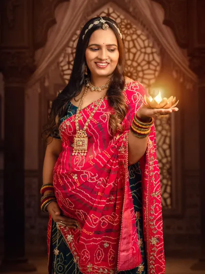 A beautiful shot of the mom-to-be holding a lit diya, the warm light illuminating her smile and traditional attire.