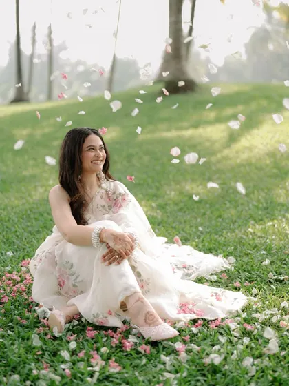 A moment of pure bliss as the bride sits on a grassy lawn, showered with flower petals, her joyful smile lighting up the frame.