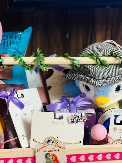 A close-up of the top tier of a sister's Rakhi hamper, showing accessories, snacks, and cute stickers like "Soul Sister" and "You are my star."
