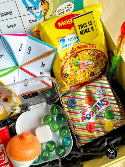 A close-up of the 90s nostalgia box, showing the 'kancha' marbles, a spinning top, Poppins, and Maggi noodles. Pure bachpan!