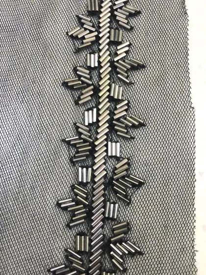 A close-up of a hand-beaded trim on a black net base. The geometric pattern is created with metallic bugle beads, offering a modern and sophisticated embellishment for gowns and western wear.