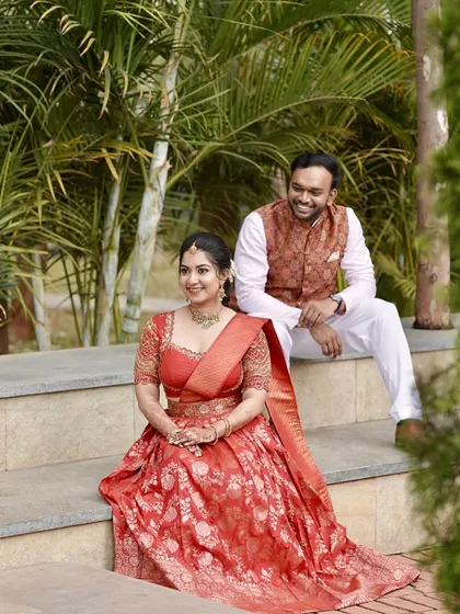 A lovely couple portrait. The bride is wearing a red half-saree, and her makeup is soft and romantic to match the engagement or pre-wedding event vibe.