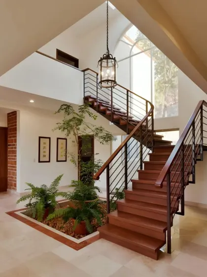 This grand entryway features a beautiful wooden staircase wrapping around a small indoor garden. The open, double-height space feels bright and connected to nature from the moment you step inside.