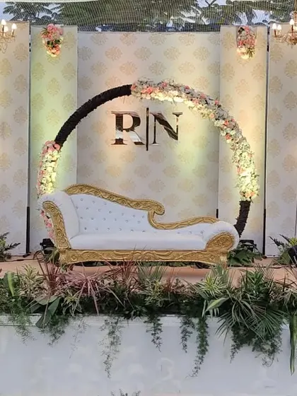A modern and elegant engagement stage featuring a circular monogrammed backdrop. The design is balanced with clean lines, minimalist candle-like lighting, and soft floral arrangements for a contemporary look.